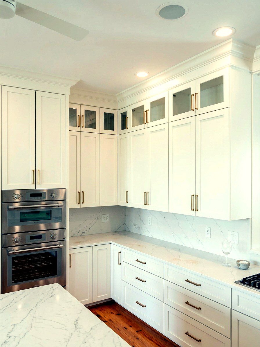 Custom white kitchen with marble countertops, glass-front upper cabinets, and stainless double ovens by Milltown Millworks